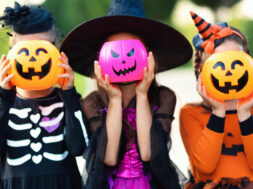 Happy Halloween! funny children in carnival costumes hide their heads behind buckets   pumpkins outdoors