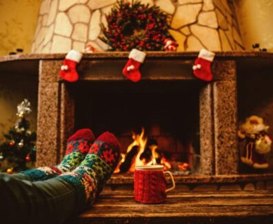 Someone-wearing-holiday-socks-relaxing-in-front-of-the-Christmas-decorated-fireplace-with-a-mug-of-hot-chocolate