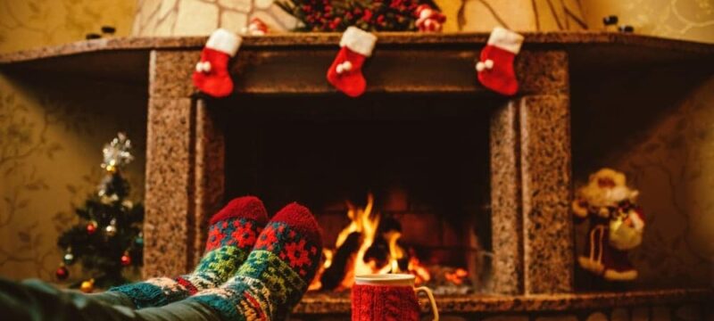 Someone-wearing-holiday-socks-relaxing-in-front-of-the-Christmas-decorated-fireplace-with-a-mug-of-hot-chocolate