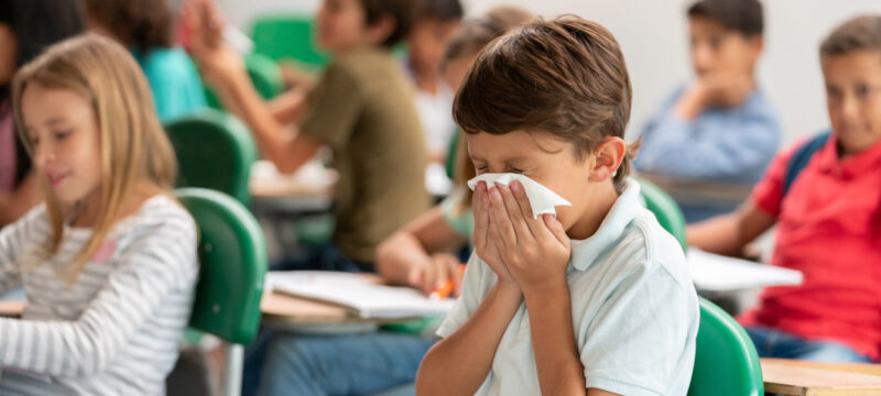 Sick boy at the school blowing his nose in class