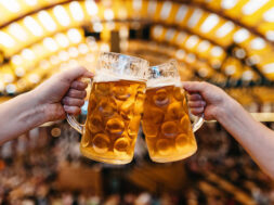 two hands clinking beer glasses in octoberfest marquee