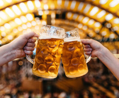 two hands clinking beer glasses in octoberfest marquee