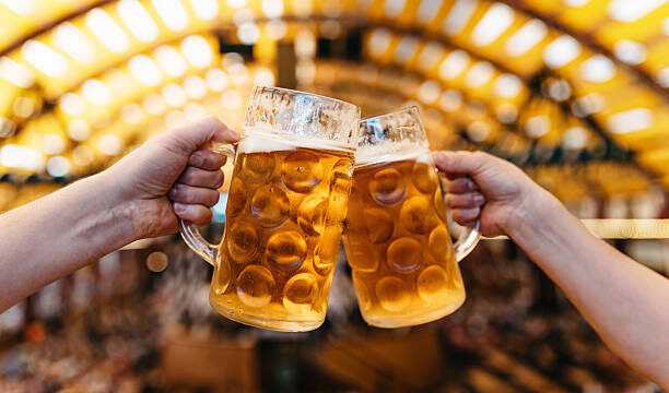 two hands clinking beer glasses in octoberfest marquee