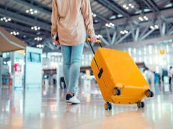 Young female traveler passenger walking with a yellow suitcase at the modern Airport Terminal, Woman on her way to flight boarding gate, Ready for travel or vacation journey