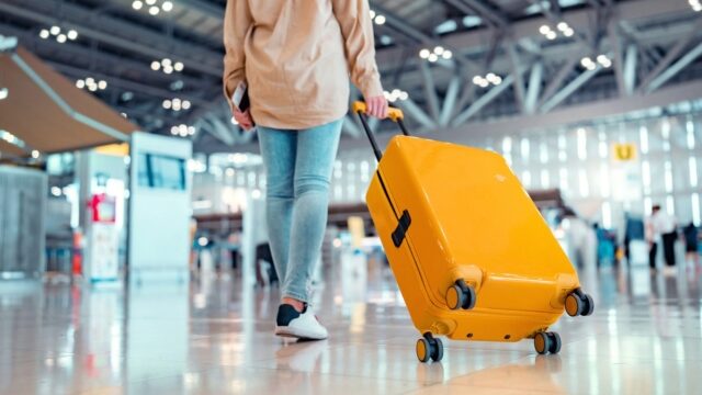 Young female traveler passenger walking with a yellow suitcase at the modern Airport Terminal, Woman on her way to flight boarding gate, Ready for travel or vacation journey