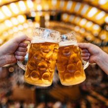 two hands clinking beer glasses in octoberfest marquee